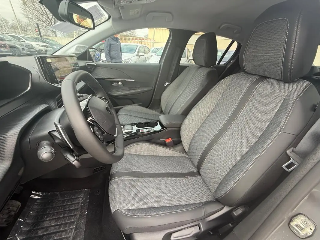 Vue intérieure côté conducteur de la Peugeot 208 Hybrid 145 Allure avec sièges gris à motifs et tableau de bord moderne.
