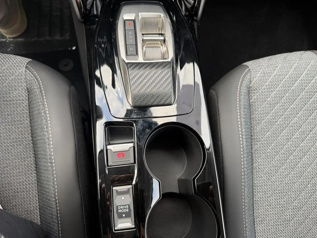 Vue plongeante sur la console centrale noire brillante de la Peugeot 208 Hybrid 145 Allure avec levier de vitesse et porte-gobelets.