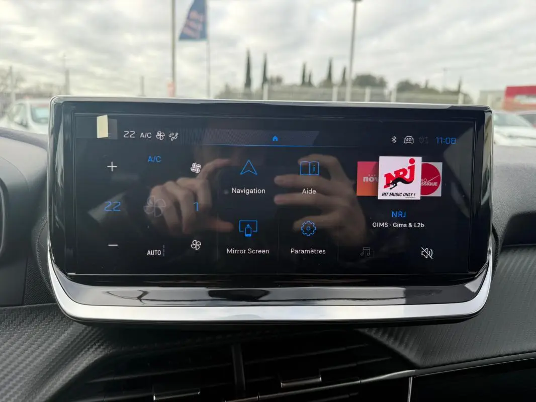 Écran tactile central du Peugeot 208 Hybrid 145 gris, affichant la radio NRJ et les options de navigation.