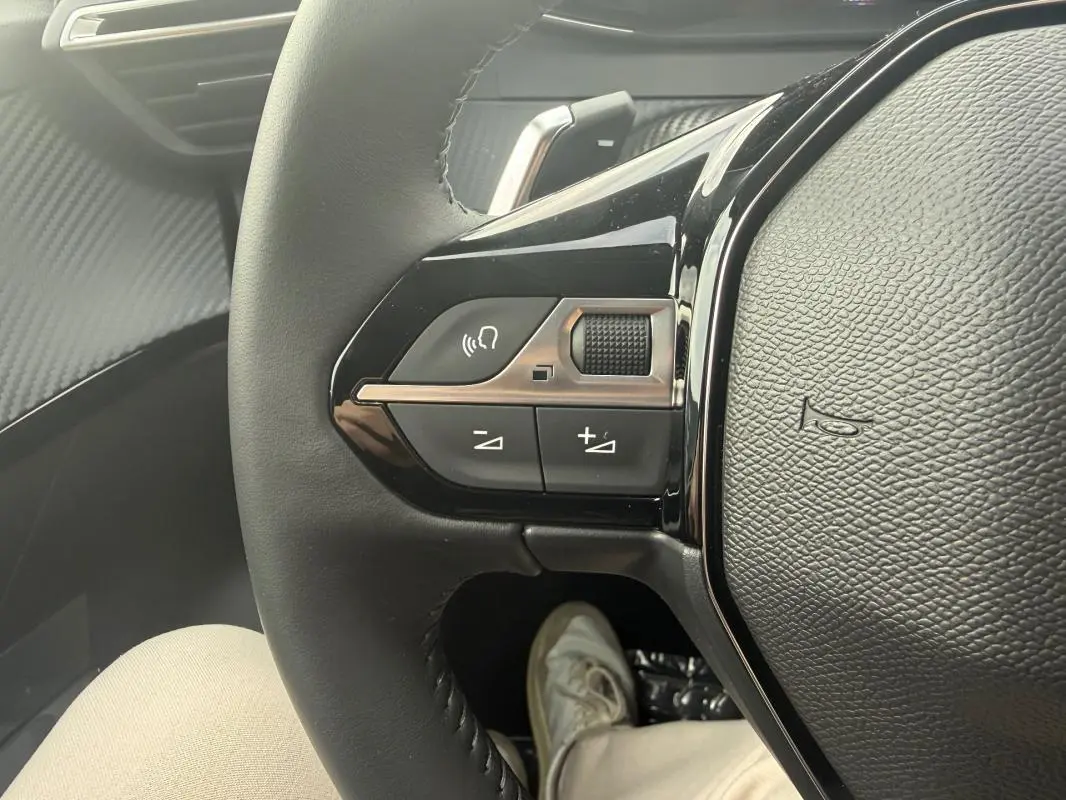 Gros plan sur les commandes du volant noir de la Peugeot 208 Hybrid 145 e-DCS6 Allure, avec détails des boutons multifonctions.