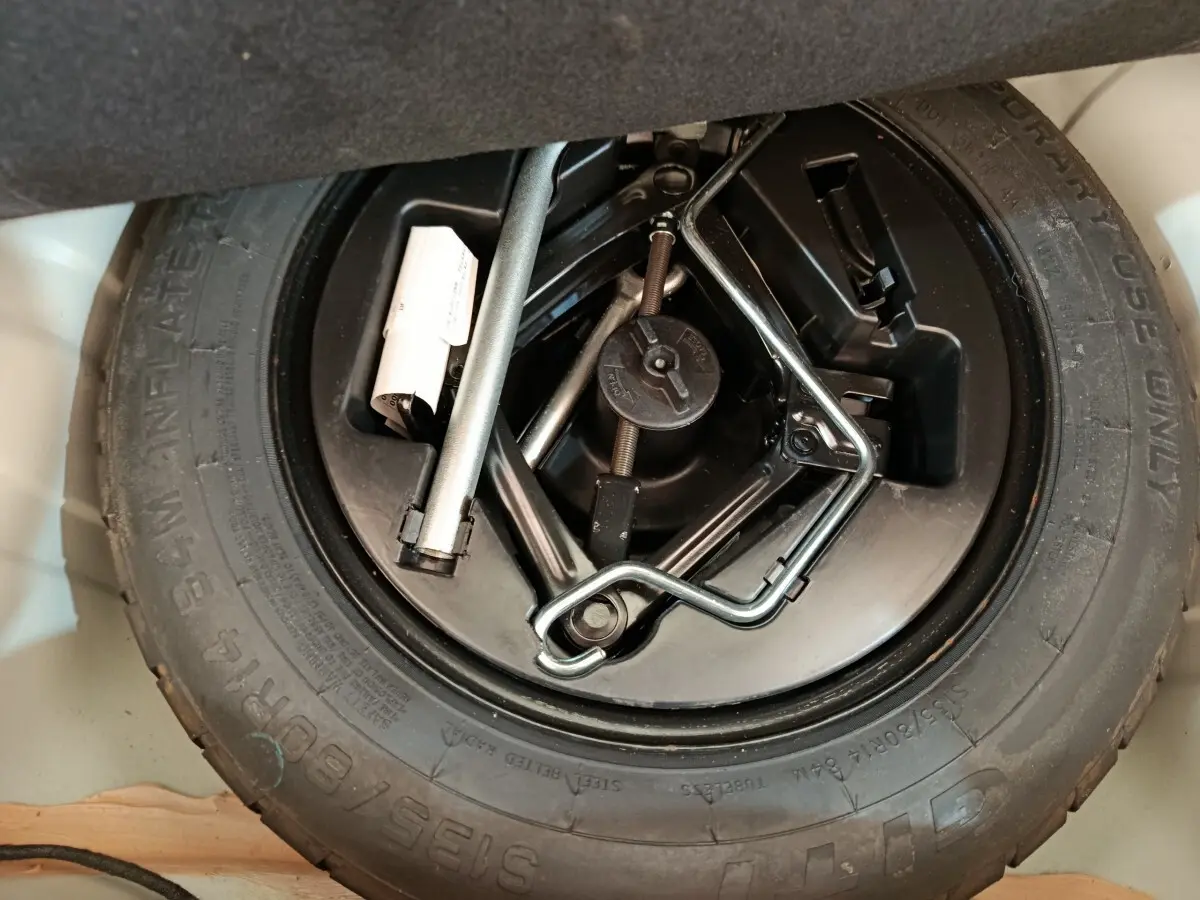 Gros plan sur la roue de secours et les outils de bord du coffre d'une Fiat 500 Hybrid blanche de 2022.
