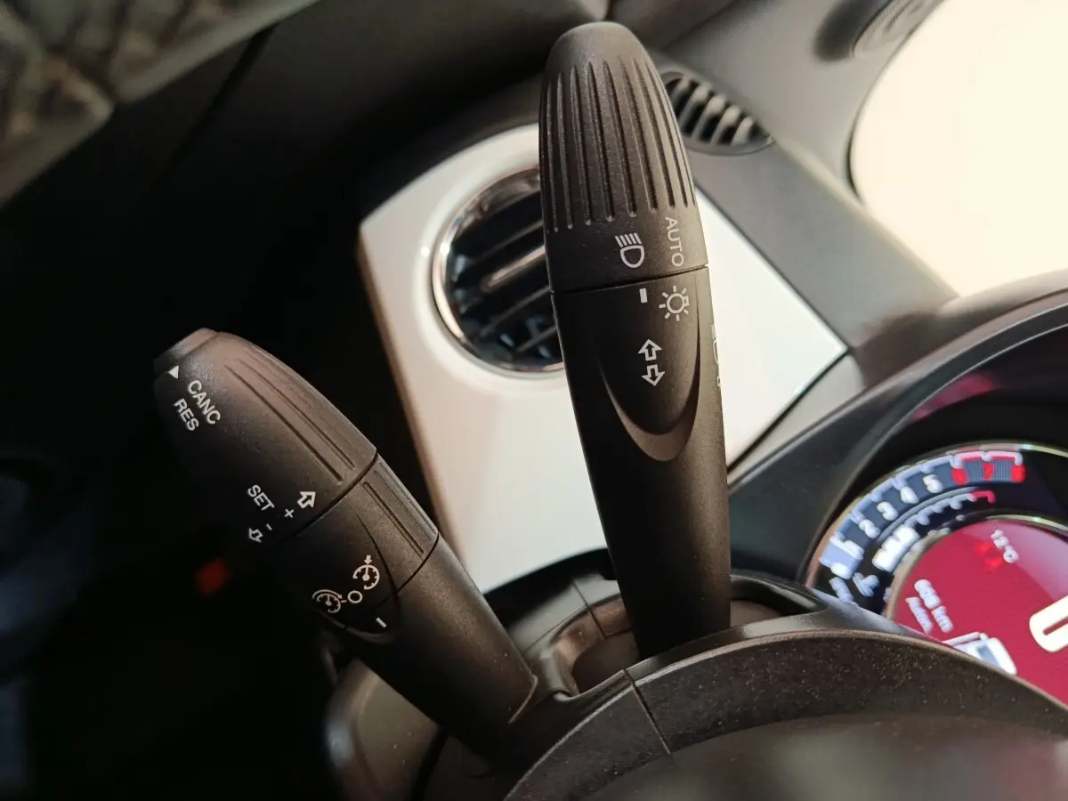 Gros plan sur les commandes de clignotants et régulateur de vitesse du tableau de bord blanc d'une FIAT 500 Hybrid 2022.