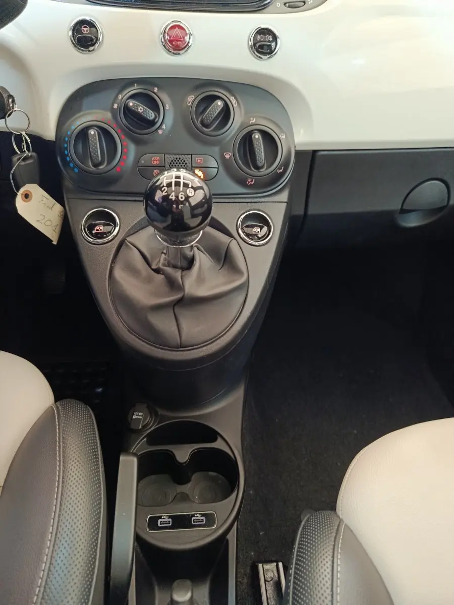 Vue intérieure centrée sur la console centrale et les commandes de climatisation d’une Fiat 500 blanche, version Hybrid.