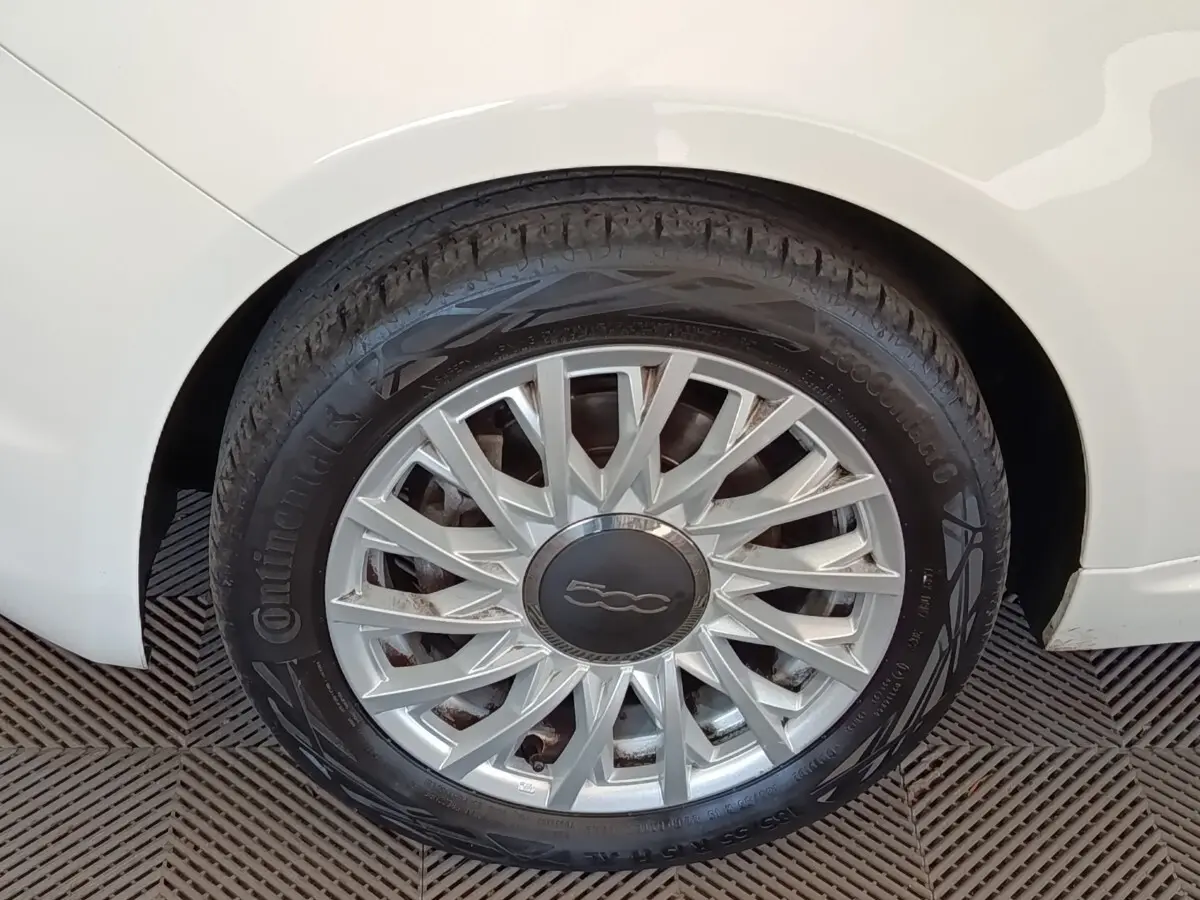 Gros plan sur la roue arrière droite d'une Fiat 500 blanche, avec jante argentée au design étoilé.