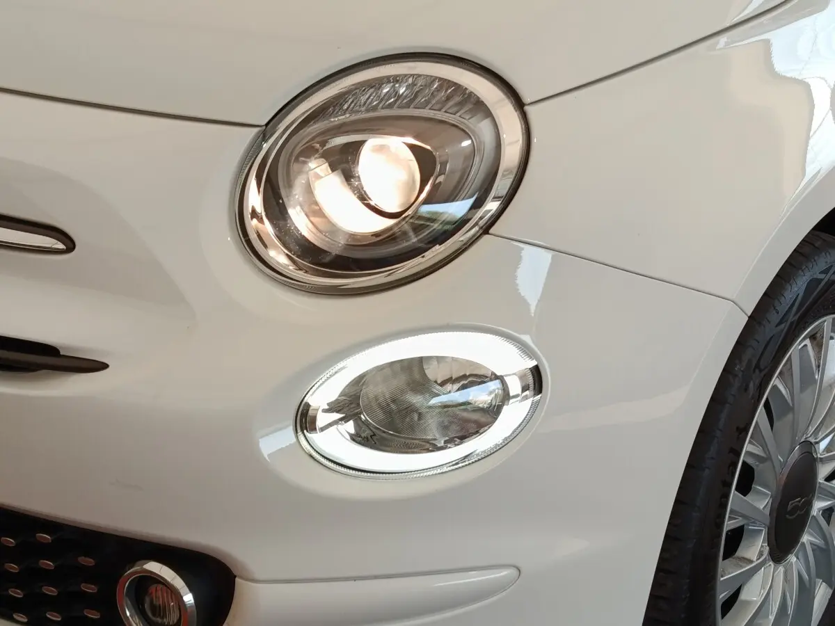 Gros plan sur l'avant droit blanc d'une FIAT 500 Hybrid 2022, mettant en valeur ses phares ellipsoïdaux et la jante distinctive.
