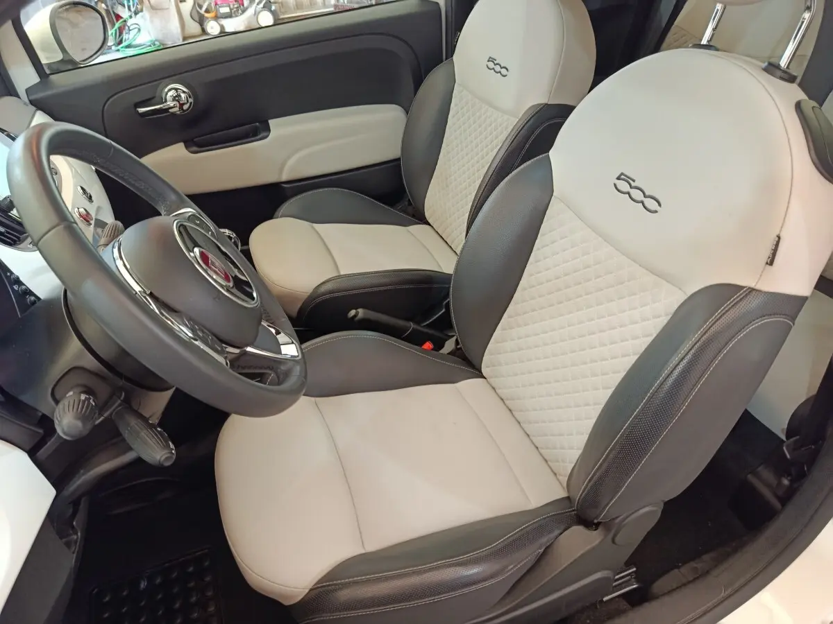 Vue intérieure côté conducteur de la Fiat 500 Dolcevita 2022 avec sièges bi-ton beige et gris et volant cuir multifonctions.