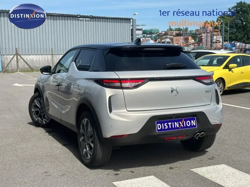 Vue 3/4 arrière droite d'une DS3 2024 Cristal Pearl avec toit noir, feux arrière fins et double sortie d'échappement chromée.
