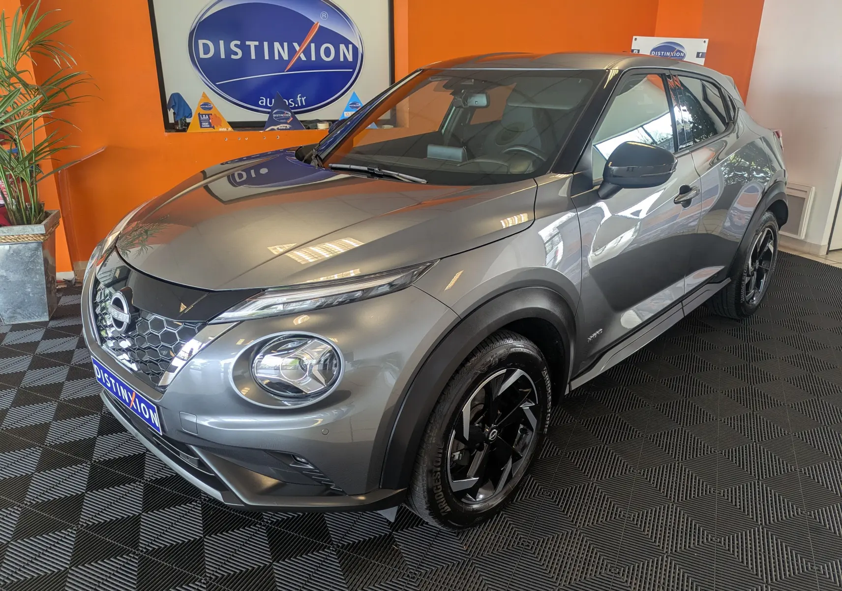 Nissan Juke 1.6 HEV gris squale métal vu en 3/4 avant droit, avec jantes noires et calandre hexagonale distinctive.