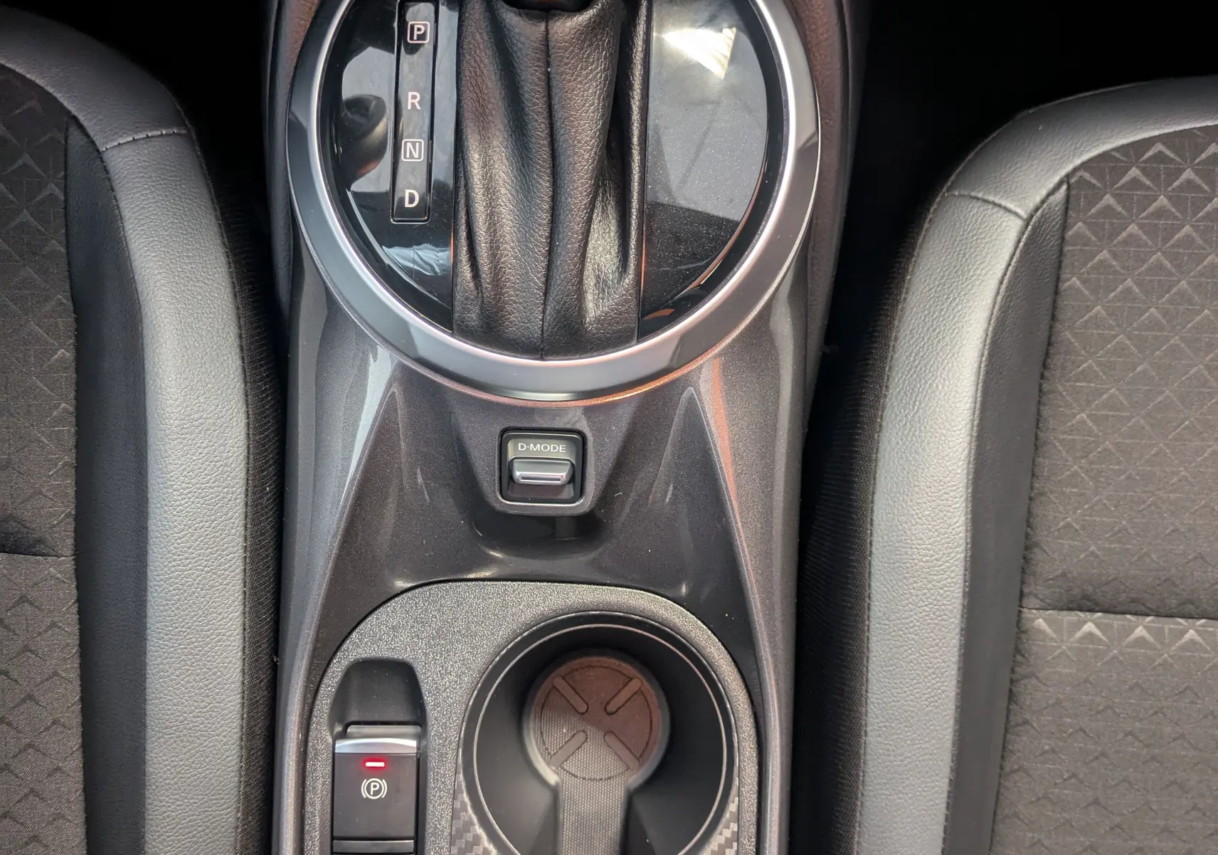 Vue plongeante sur la console centrale noire du Nissan Juke gris, avec levier de vitesses automatique et porte-gobelets.