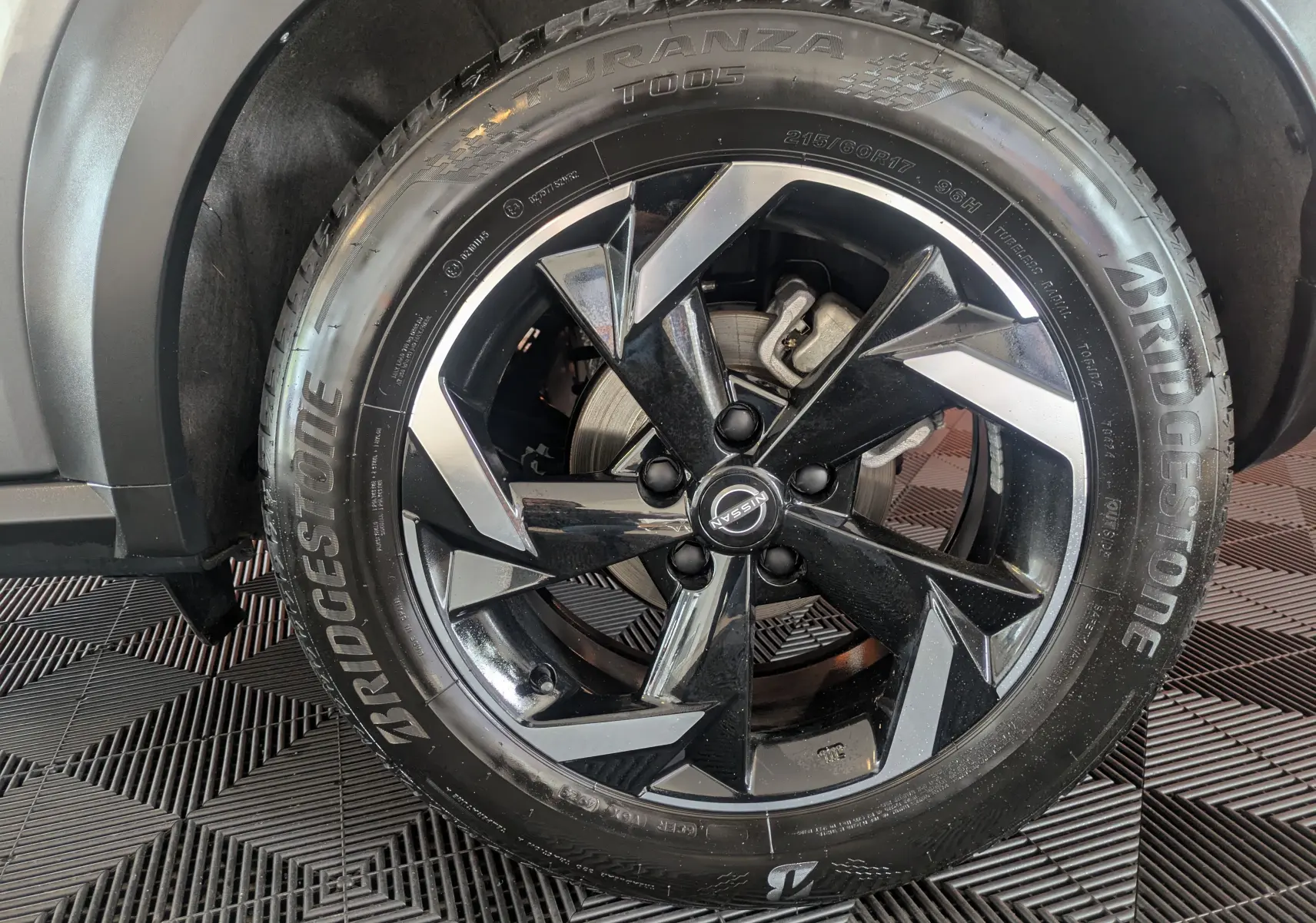 Gros plan sur la roue avant droite du Nissan Juke 2024 gris squale métal, avec jante alliage noire et détails argentés.