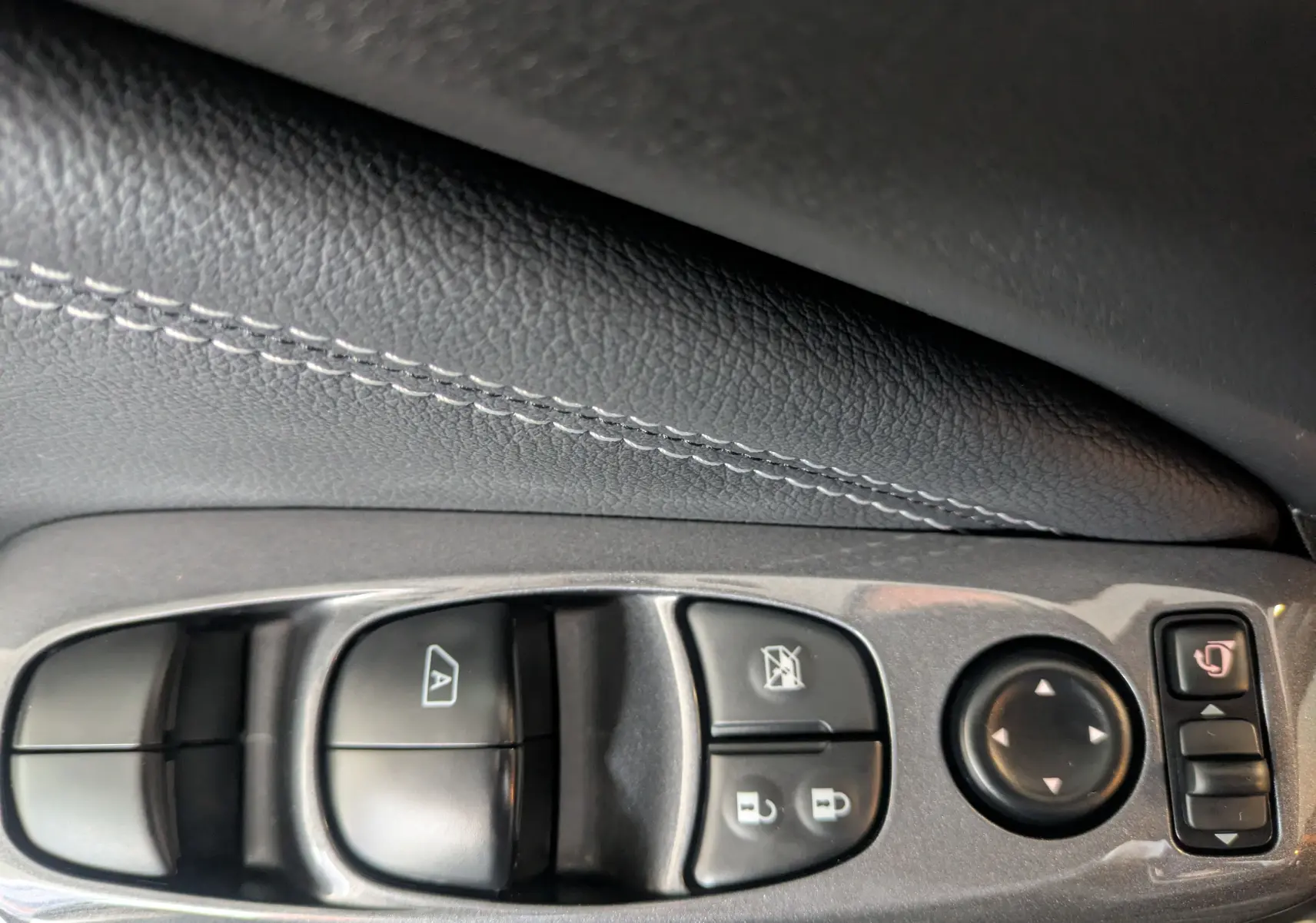 Gros plan sur les commandes de lève-vitres et rétroviseurs côté conducteur du Nissan Juke gris squale métal 2024.