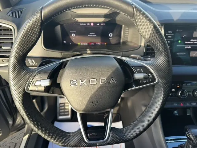 Vue rapprochée du volant perforé SKODA avec tableau de bord digital et commandes intégrées, intérieur gris du Karoq 2025.