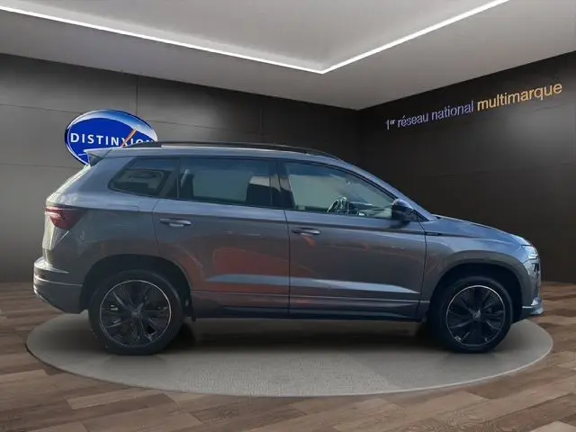 Vue de profil côté gauche du Skoda Karoq gris graphite 2025 avec jantes alliage noires et attelage escamotable visible.