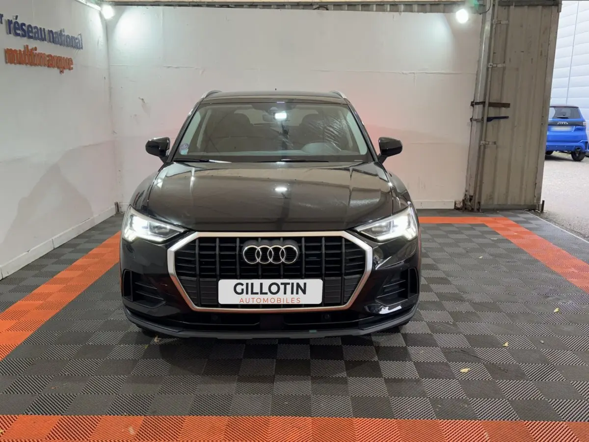 Audi Q3 noir vue de face dans un garage, avec calandre hexagonale chromée et phares LED allumés.