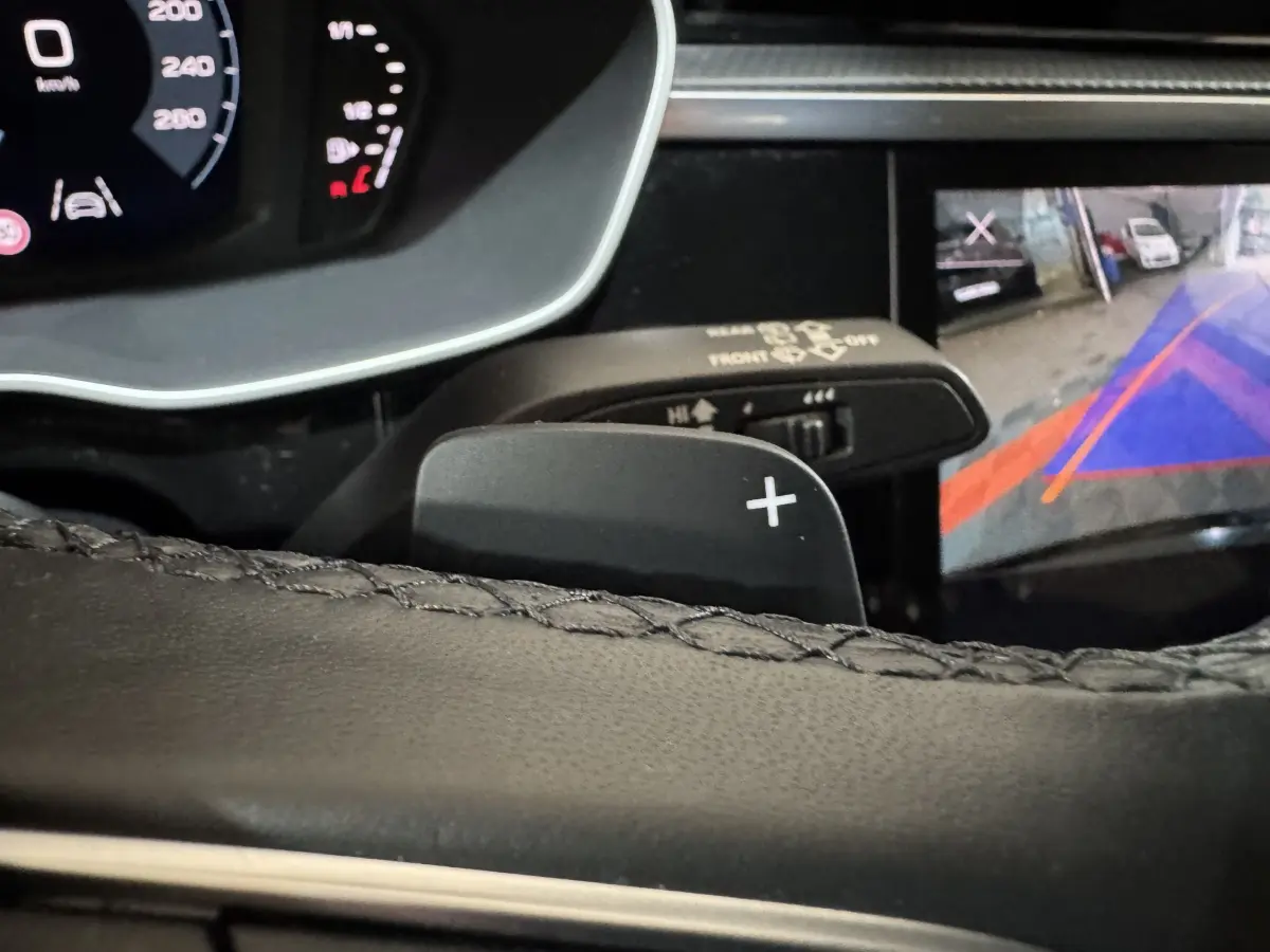 Détail du levier de vitesse au volant et écran de caméra de recul dans l'Audi Q3 noir 2022, vue intérieure rapprochée.