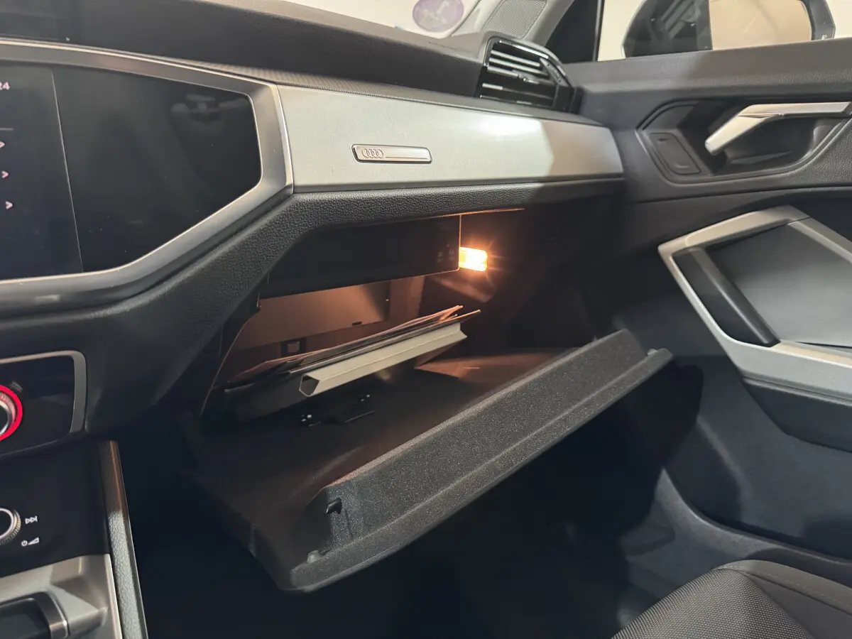 Intérieur Audi Q3 35 TFSI 2022 côté passager, boîte à gants ouverte avec éclairage et tableau de bord noir.