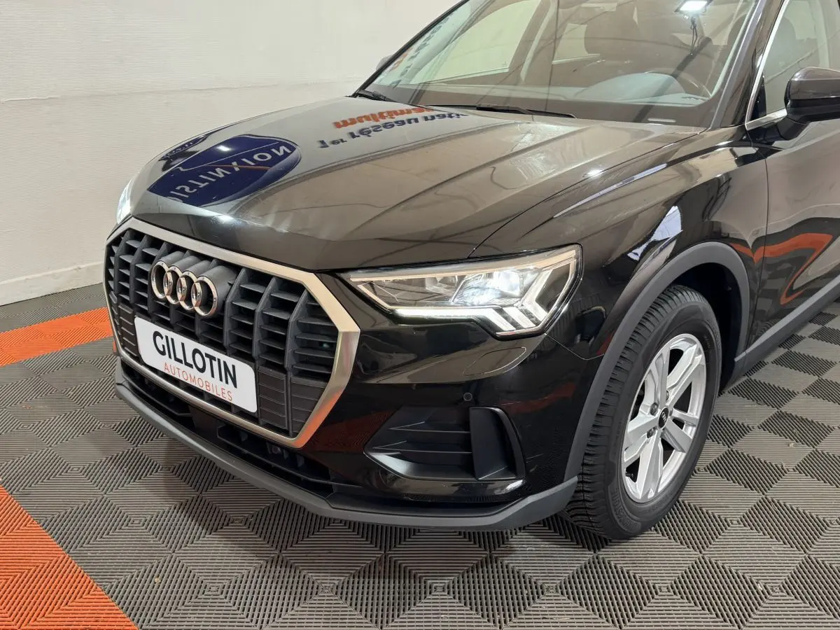 Vue 3/4 avant droit d'un Audi Q3 noir 2022 avec calandre hexagonale et phares LED allumés en intérieur showroom.