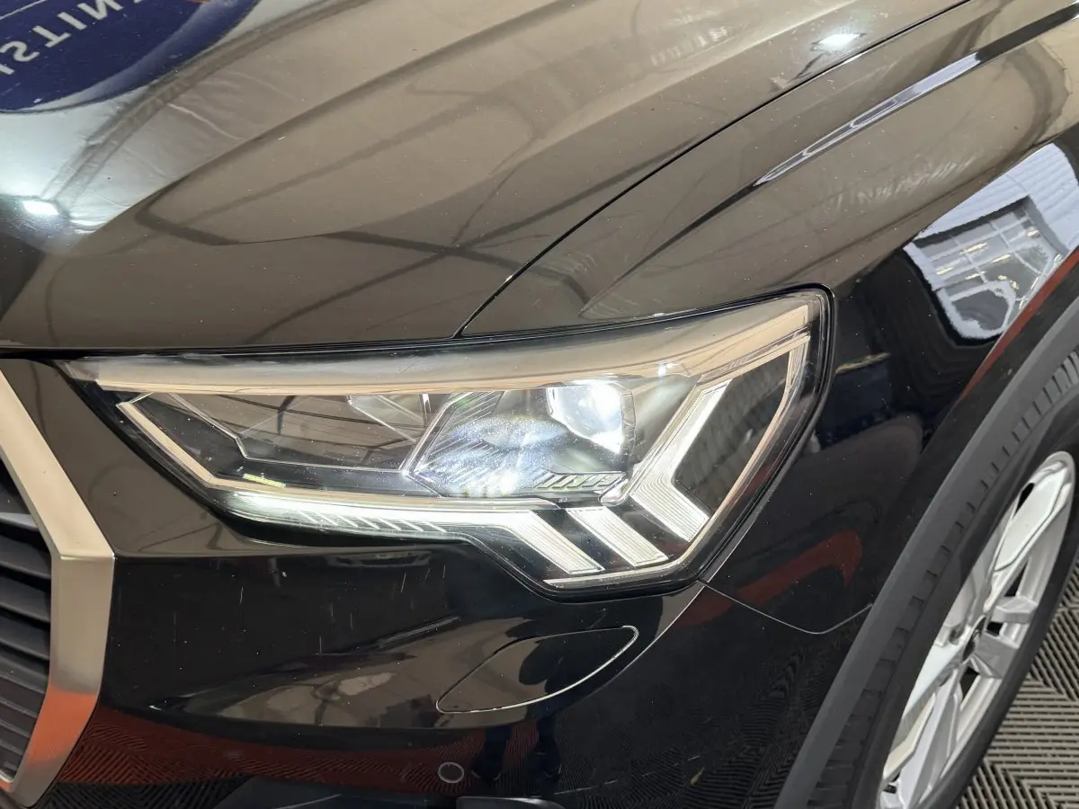 Gros plan sur le phare avant droit du SUV Audi Q3 noir, mettant en valeur son design LED distinctif.