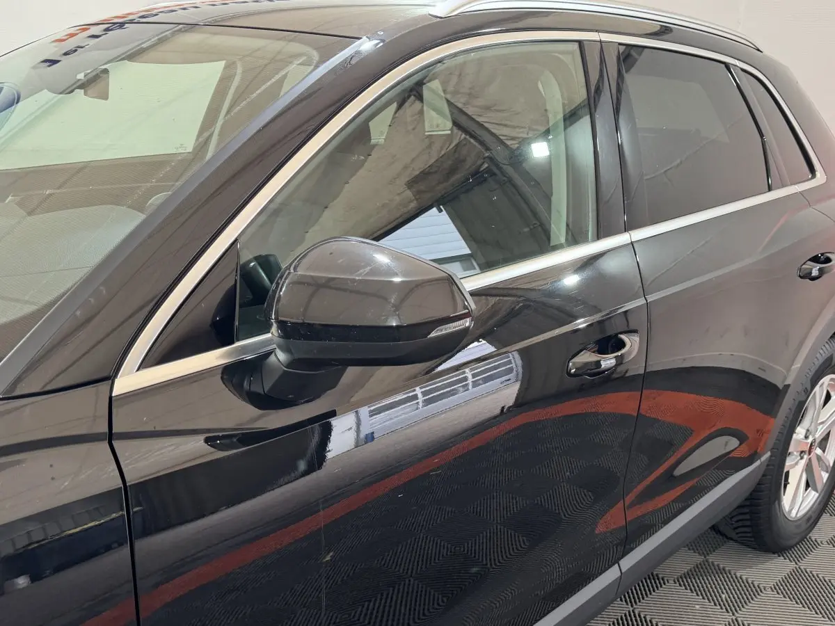 Vue latérale côté gauche d'un Audi Q3 noir brillant avec rétroviseur et poignées de porte visibles.