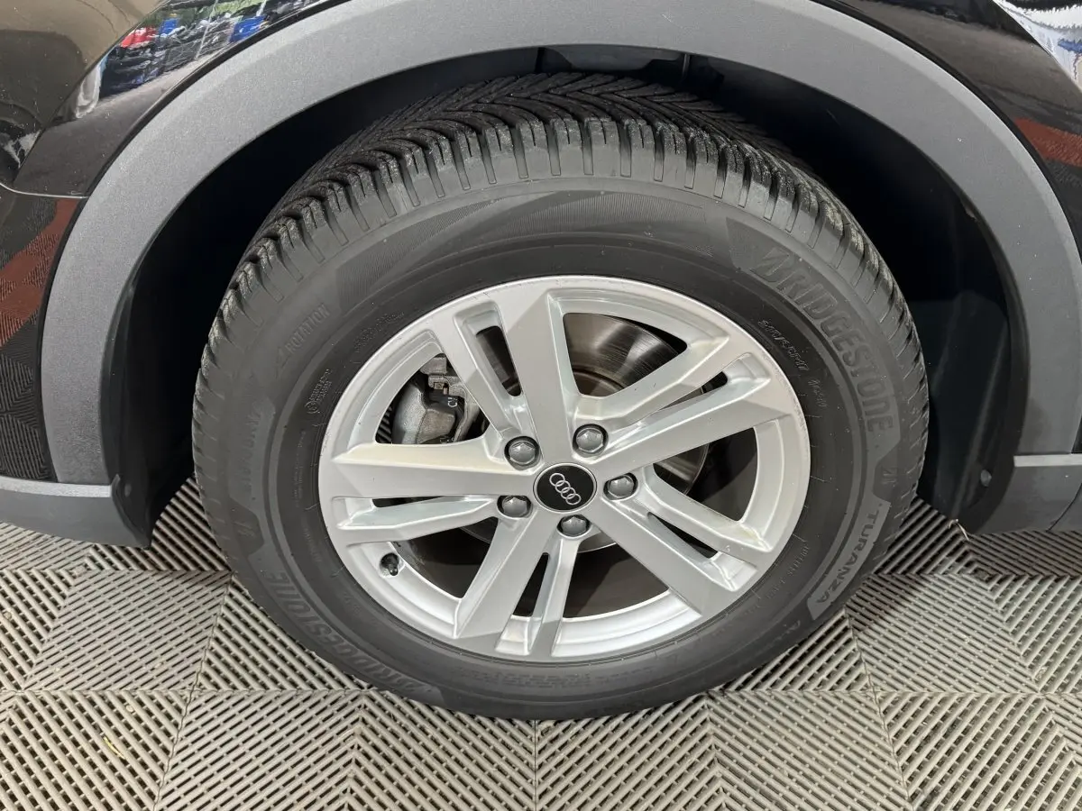 Gros plan sur la roue avant gauche noire de l'Audi Q3 35 TFSI avec jante argentée à 5 branches doubles.