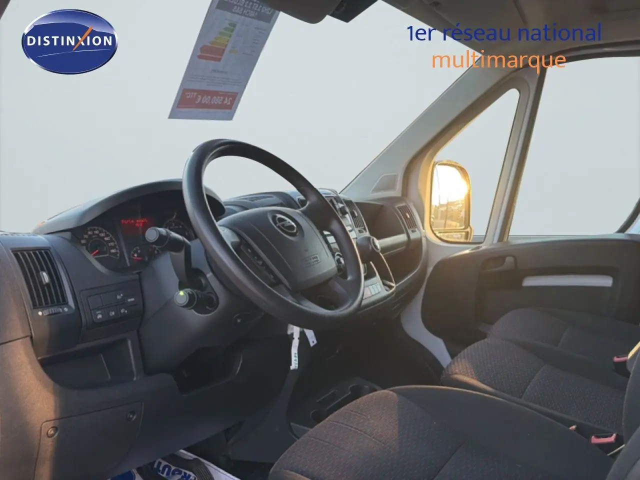 Vue intérieure côté conducteur de l'Opel Movano Fourgon blanc Icy 2023, avec tableau de bord et sièges en tissu noir.