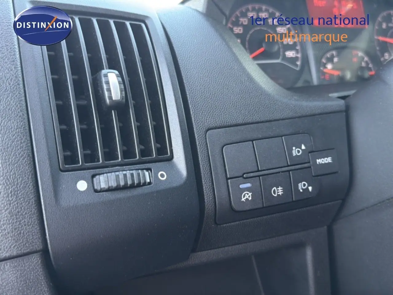 Détail intérieur montrant la grille d'aération et les commandes d'éclairage du tableau de bord d'un Opel Movano blanc.