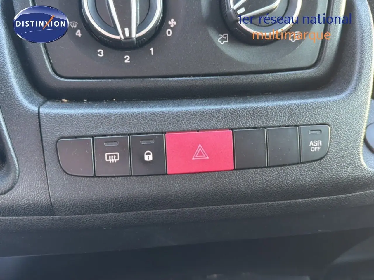 Gros plan sur la console centrale noire de l'Opel Movano Fourgon 2023, avec boutons de sécurité et climatisation.