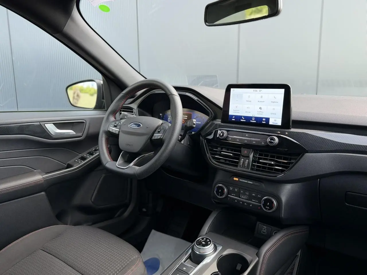 Vue intérieure côté conducteur du Ford Kuga 2023, tableau de bord noir avec écran tactile et volant ST-Line à surpiqûres rouges.