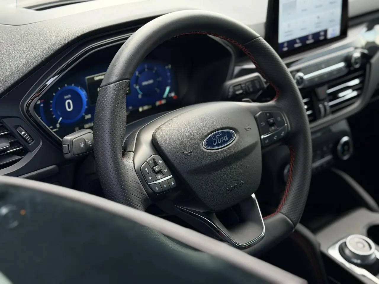 Vue rapprochée du volant noir avec surpiqûres rouges du Ford Kuga 2.0 EcoBlue 120 BVA ST-Line 2023 et tableau de bord numérique.