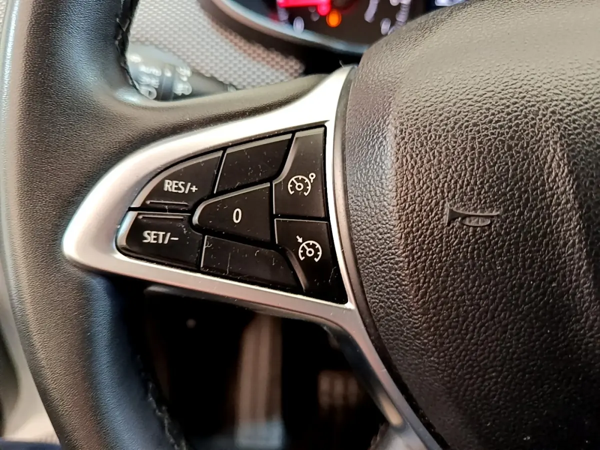 Gros plan sur le côté gauche du volant noir de la Dacia Sandero blanc, avec commandes de régulateur de vitesse.