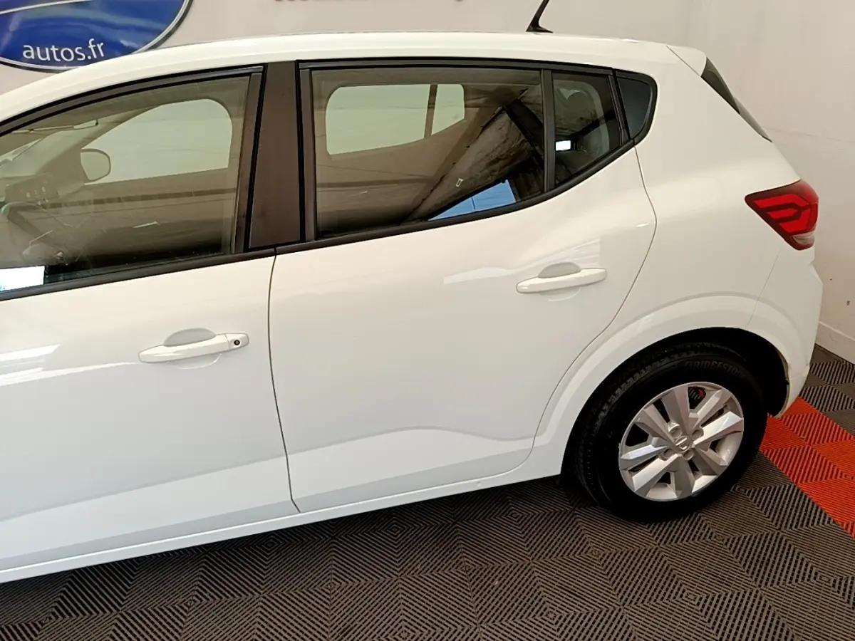 Vue latérale droite d'une Dacia Sandero blanche 2022, mettant en valeur les poignées de porte et la jante alliage.