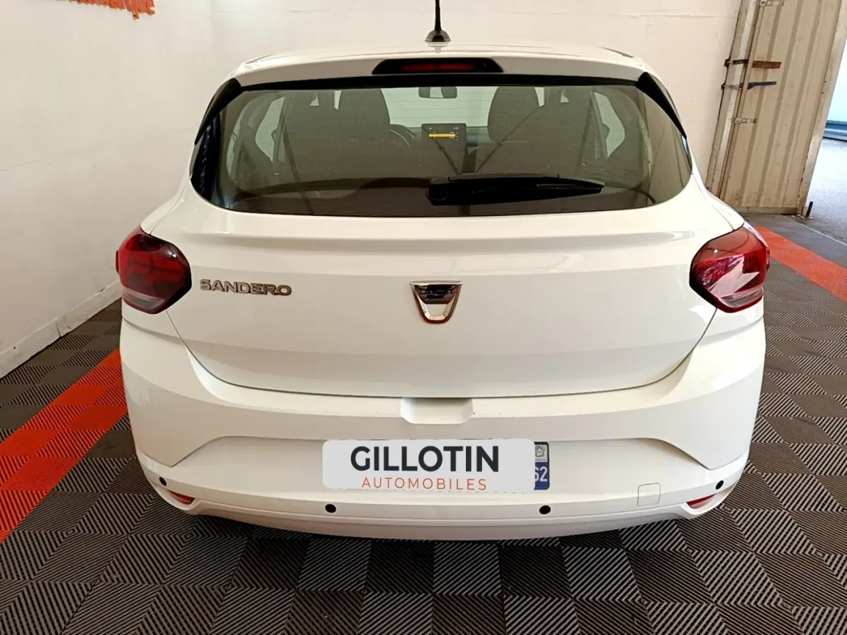 Vue arrière d'une Dacia Sandero blanche 2022 avec feux arrière rouges et logo central sur un sol à motifs.