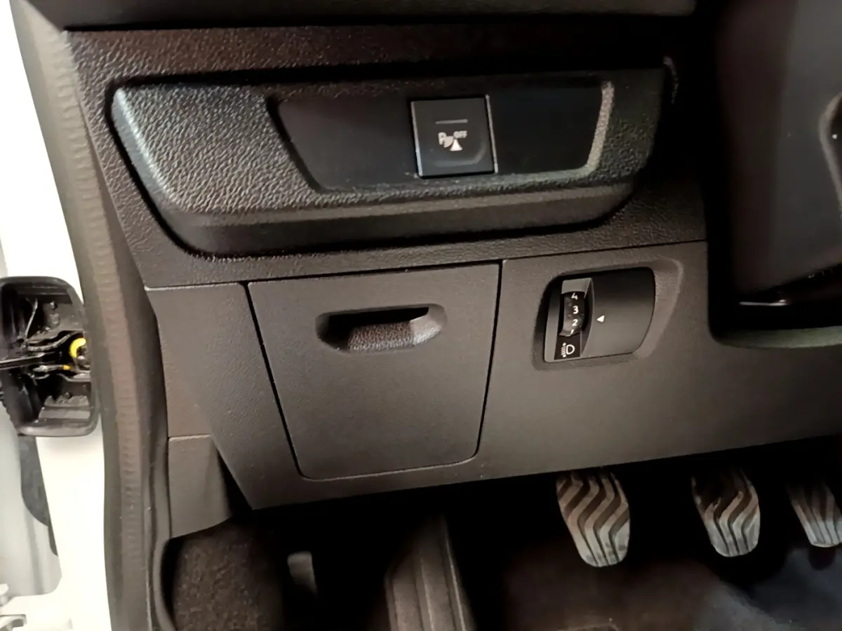 Détail intérieur côté gauche montrant les commandes de réglage des phares et désactivation du système d'aide au stationnement sur Dacia Sandero blanc.