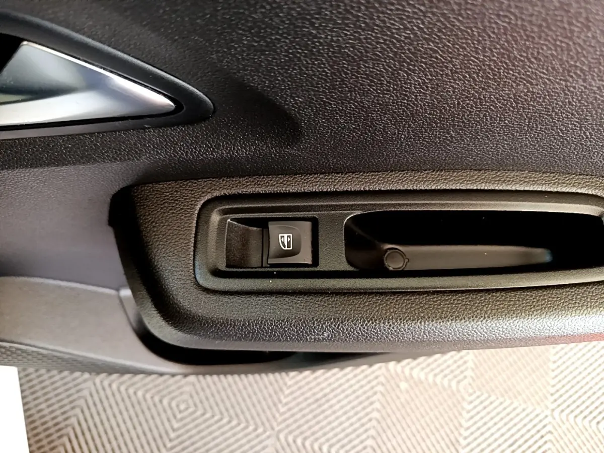 Gros plan sur la commande de lève-vitre noir dans la portière intérieure d'une Dacia Sandero blanche.