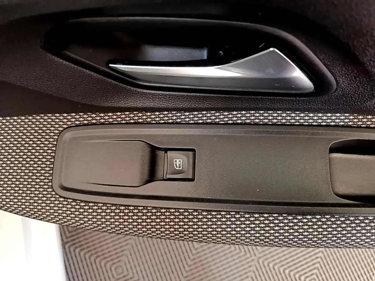 Détail de la commande de lève-vitre côté conducteur sur la porte intérieure d'une Dacia Sandero blanche, tissu gris.
