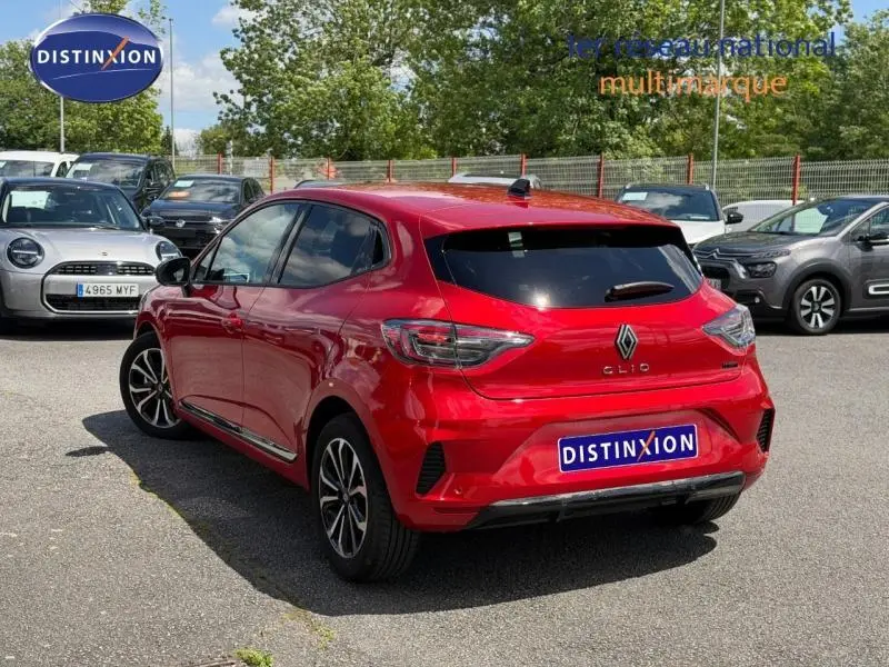 Vue 3/4 arrière d'une Renault Clio 1.6 E-Tech 145ch full hybrid rouge flamme avec jantes alliage, stationnée en extérieur.