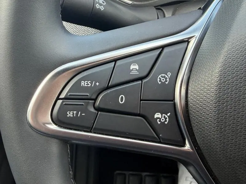 Gros plan sur les commandes noires du volant côté gauche de la Renault Clio 1.6 E-Tech Rouge Flamme, avec boutons de régulateur de vitesse.