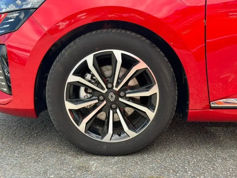 Gros plan sur la roue avant gauche d'une Renault Clio 1.6 E-Tech rouge flamme avec jante alliage au design moderne.