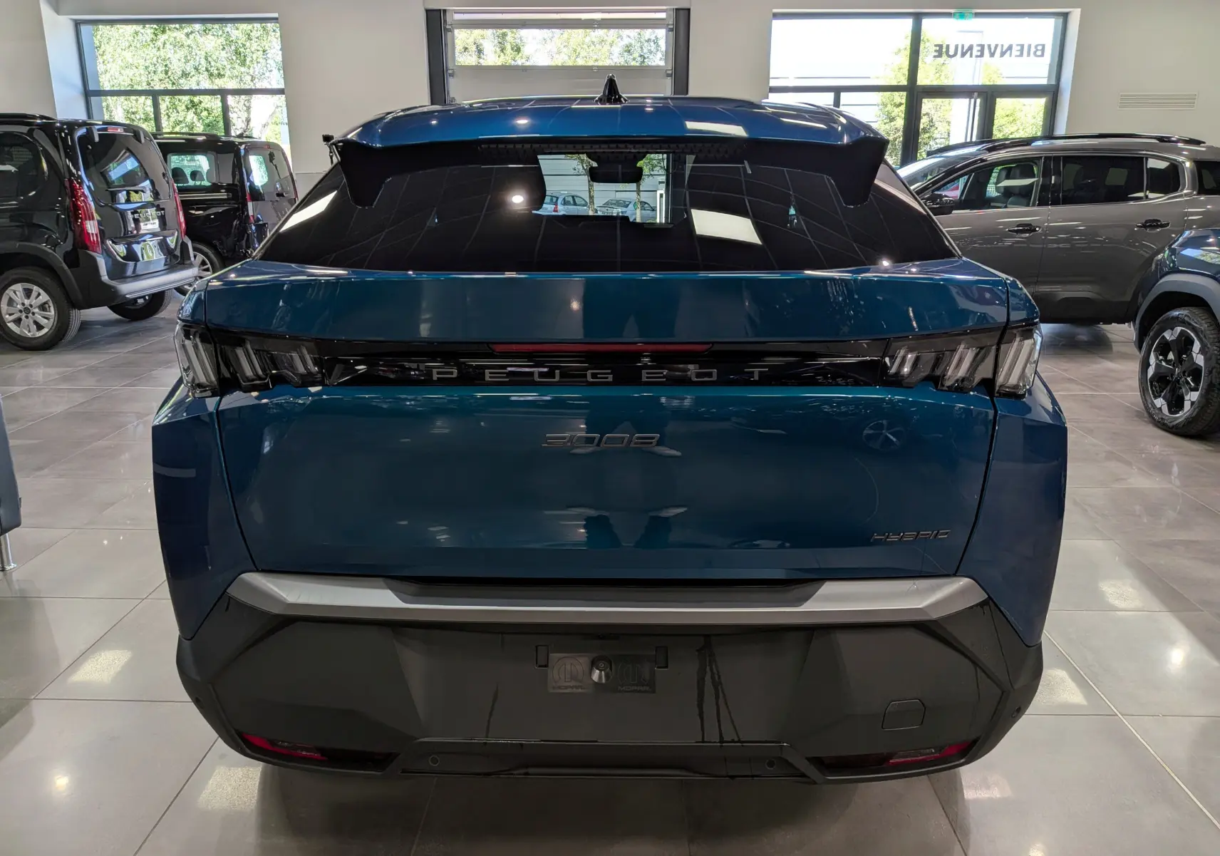 Vue arrière d’un Peugeot 3008 Hybrid bleu Obsession, avec feux arrière distinctifs en forme de griffes et logo central lumineux.