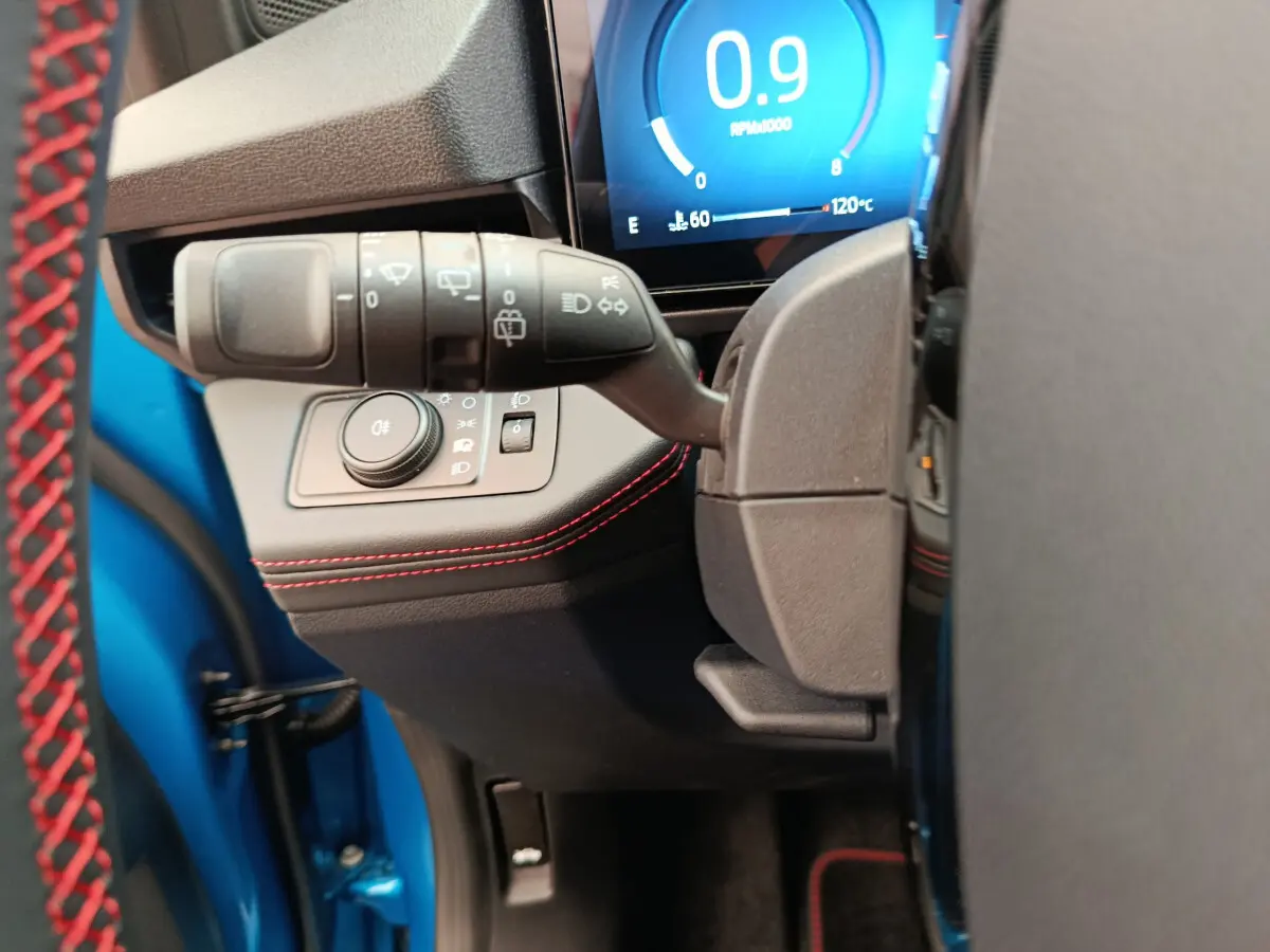 Détail du commodo d'éclairage et tableau de bord numérique du Ford Puma bleu, côté gauche avec surpiqûres rouges.