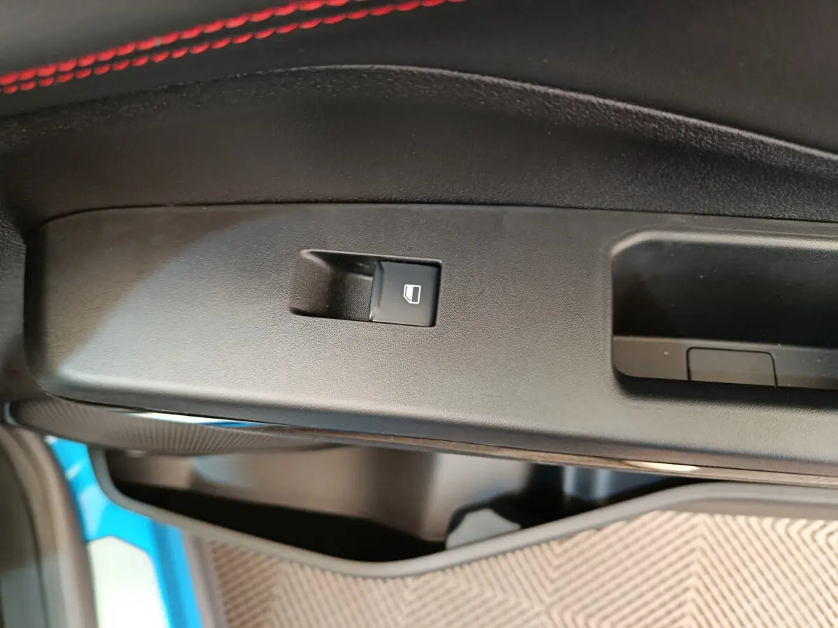 Bouton de commande de lève-vitre sur la porte intérieure noire du Ford Puma bleu, détail côté conducteur.