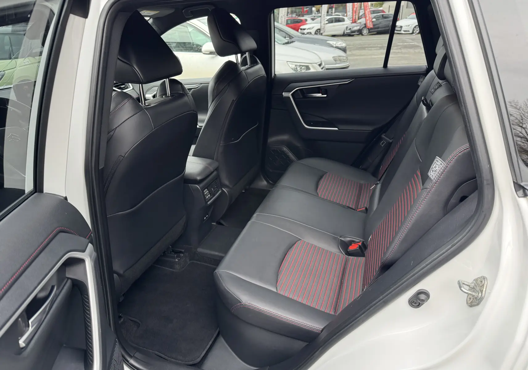 Vue intérieure arrière côté droit du Suzuki Across blanc 2023, sièges noirs avec surpiqûres rouges et détails modernes.