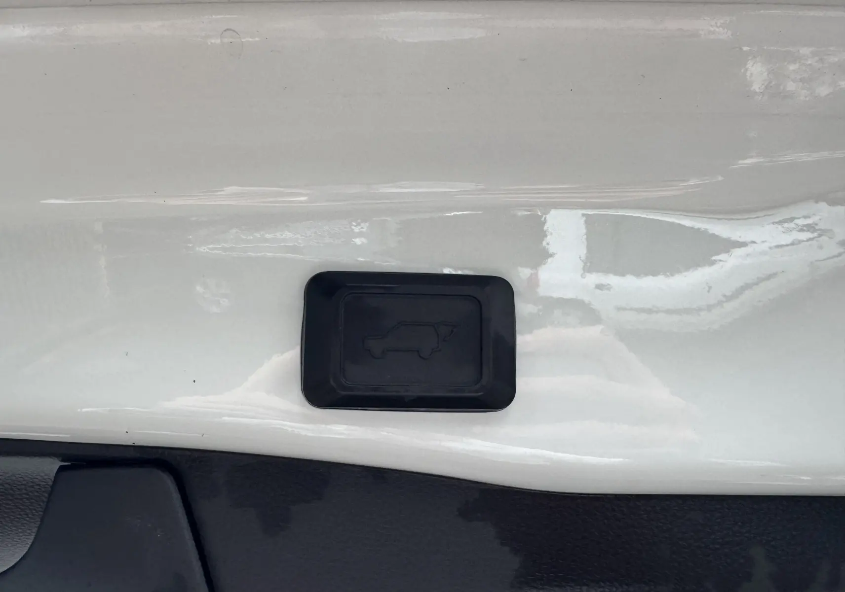 Gros plan sur le bouton noir d'ouverture du coffre sur la carrosserie blanche du Suzuki Across hybride rechargeable 2023.