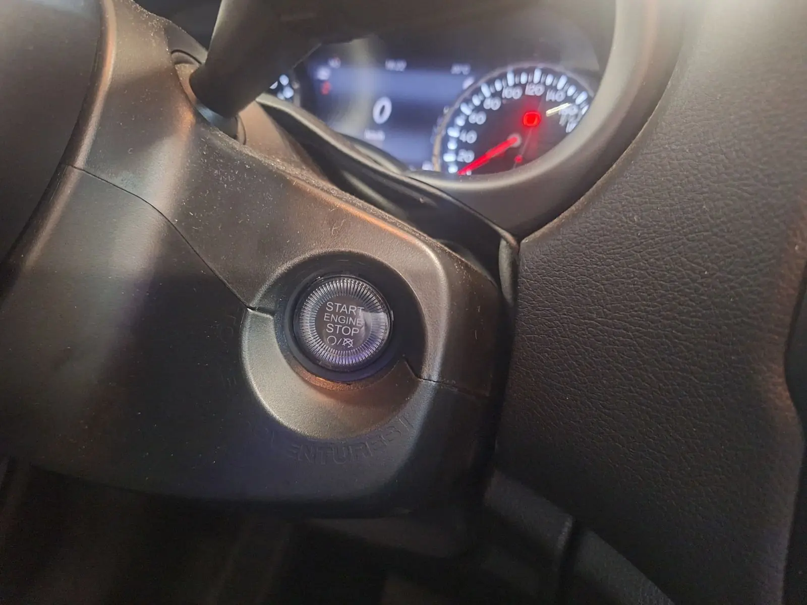 Bouton start/stop moteur en gros plan sur le tableau de bord noir du Jeep Renegade 2024, avec compteurs en arrière-plan floutés.