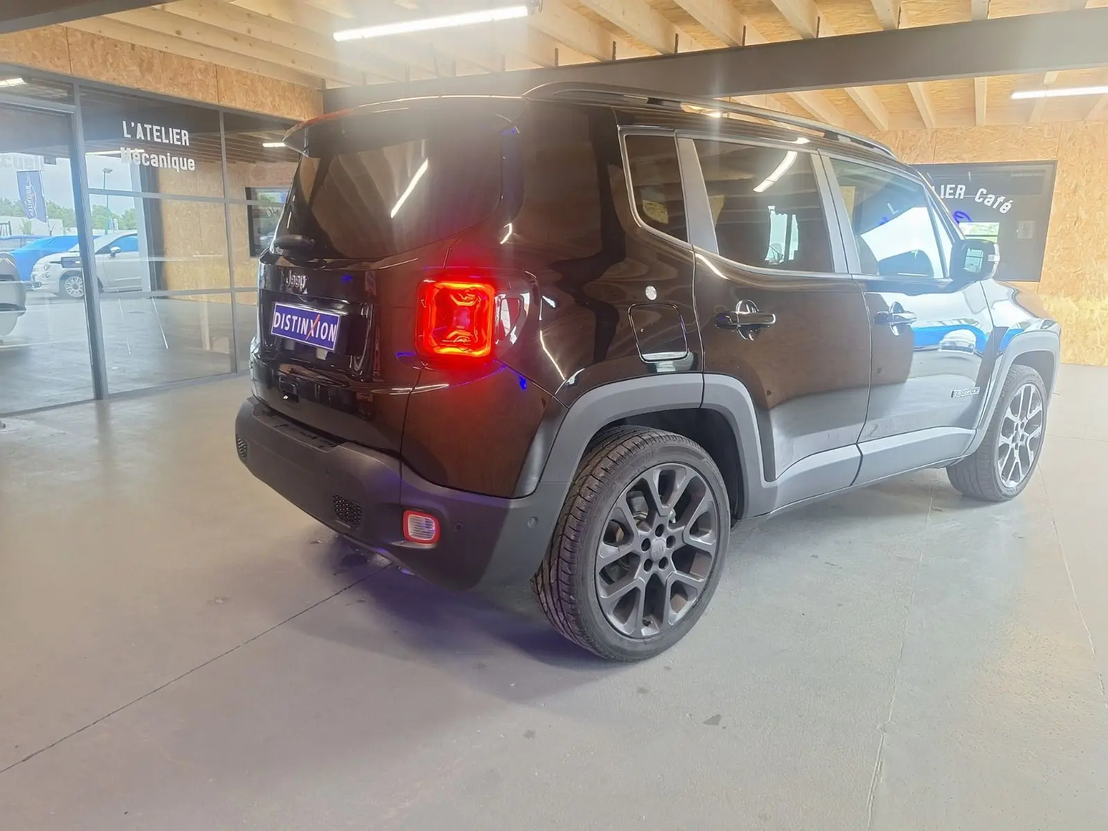 Jeep Renegade noir en vue 3/4 arrière droit, avec feux arrière allumés et jantes alliage 19 pouces visibles.