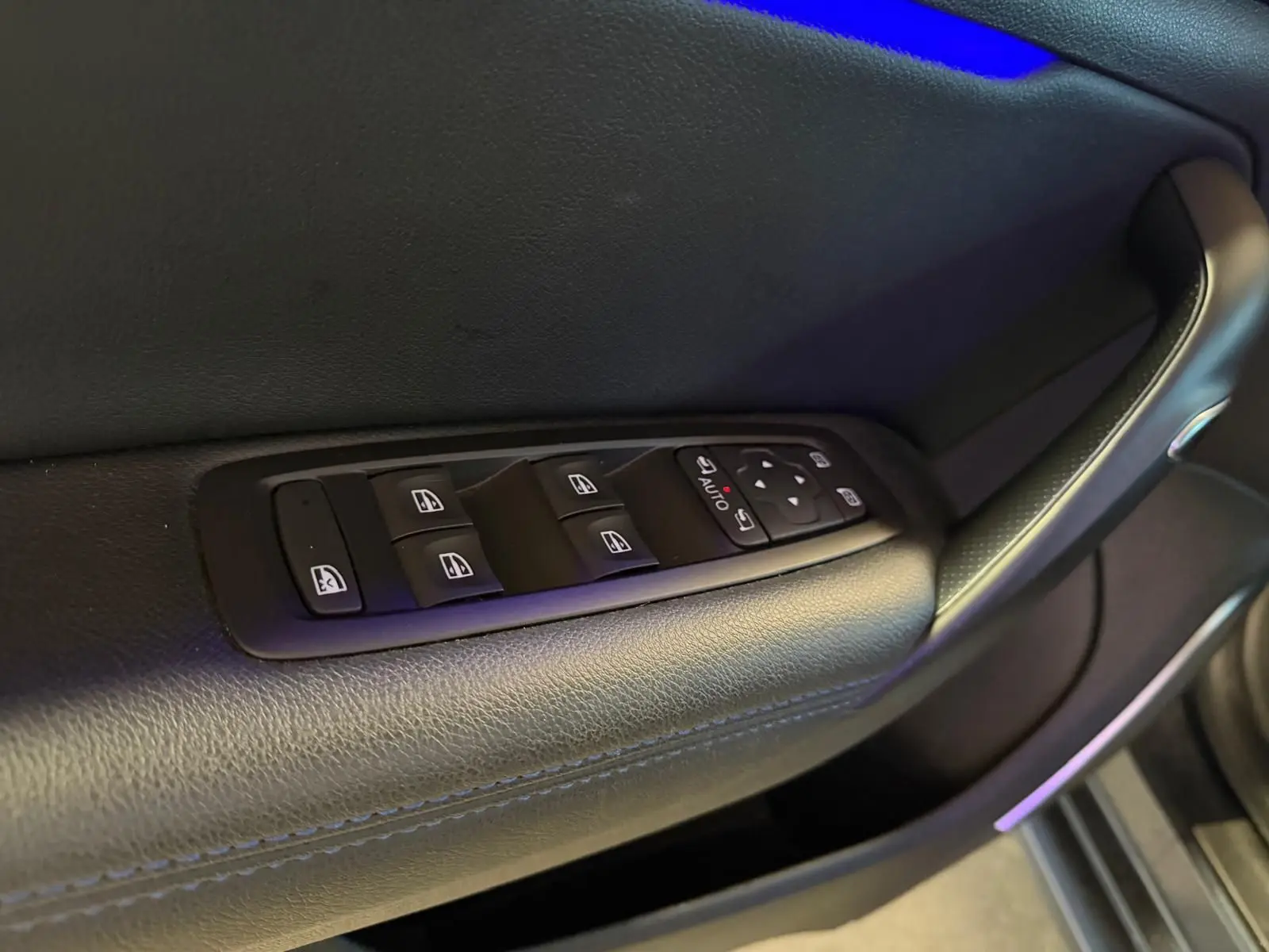 Gros plan sur la commande des vitres électriques côté conducteur de la Renault Mégane Break gris, intérieur cuir noir.