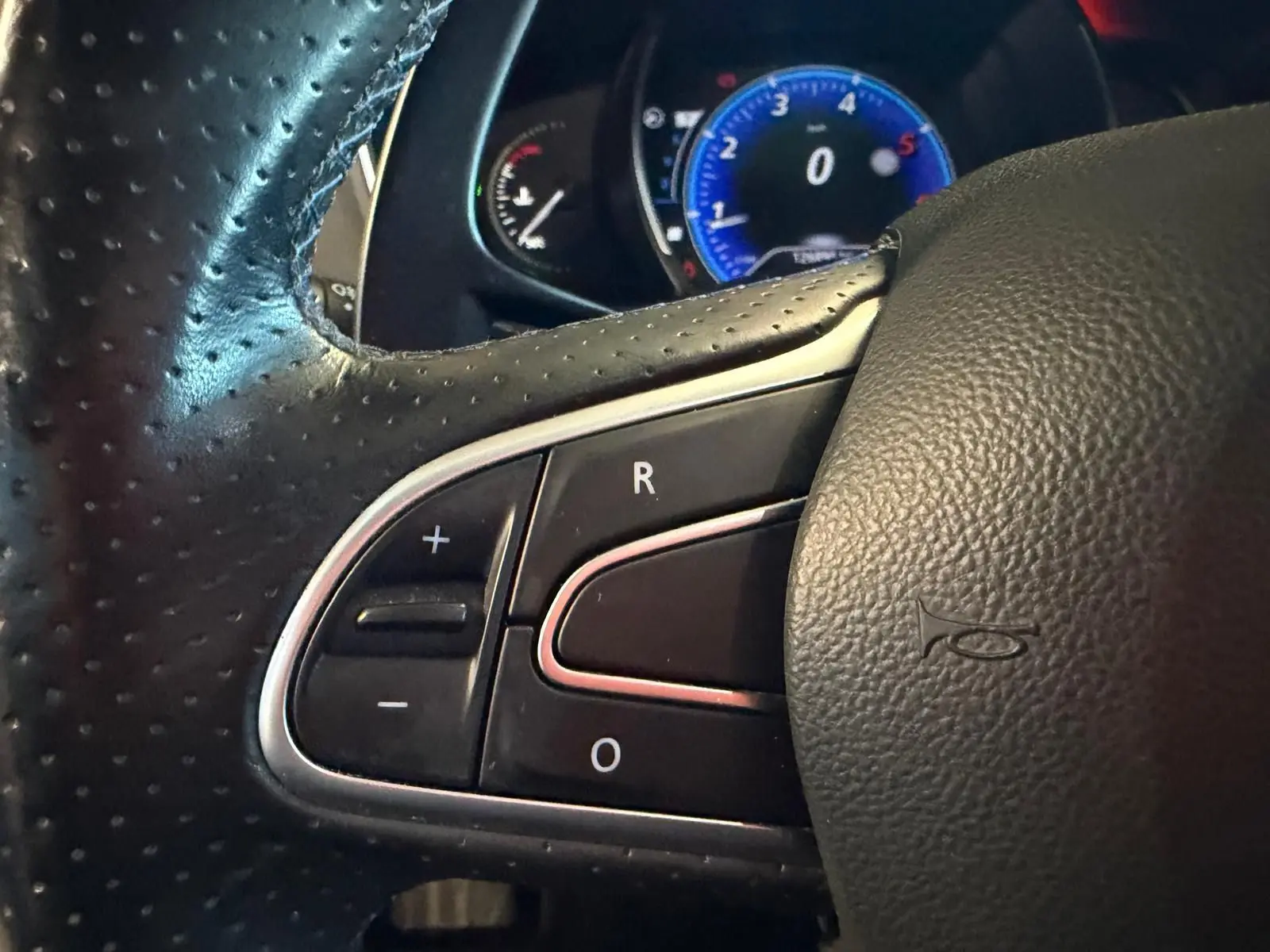 Gros plan sur le volant en cuir noir de la Renault Mégane Break GT 2017, avec commandes intégrées et tableau de bord bleu en arrière-plan.