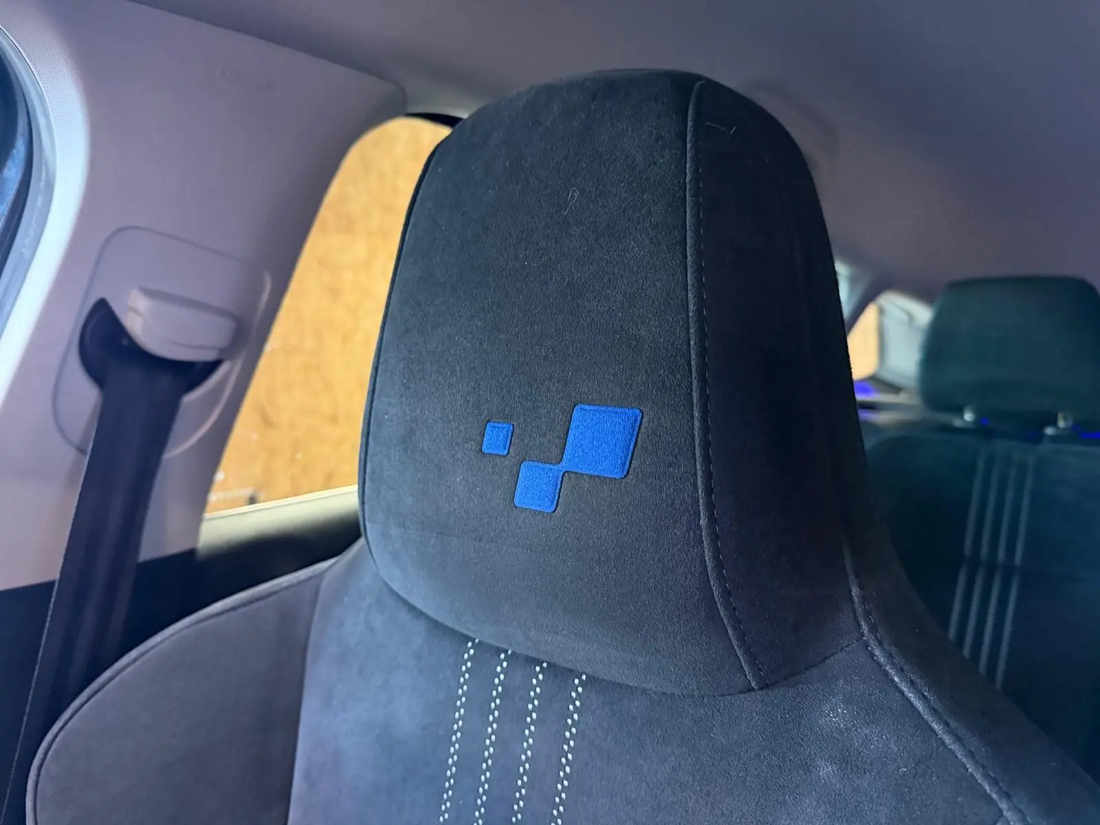 Gros plan sur l’appui-tête avant noir en tissu avec logo bleu, intérieur de la Renault Mégane Break GT 2017.