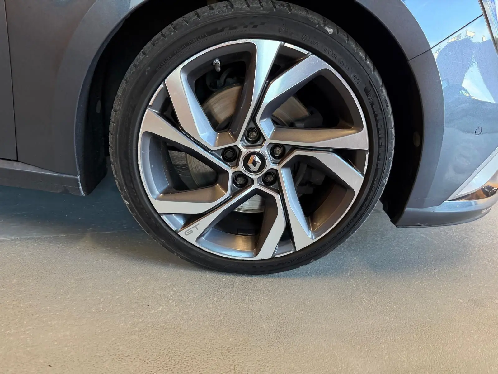 Gros plan sur la roue avant droite grise d'une Renault Mégane Break GT 2017 avec jante alliage marquée GT.