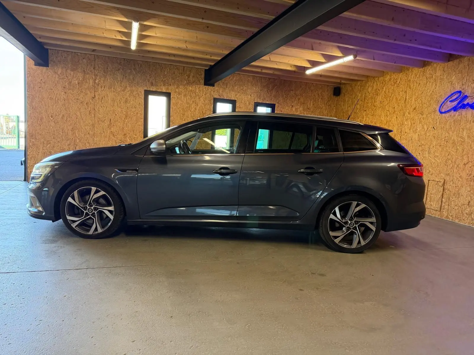 Renault Mégane Break GT gris vue de profil côté gauche, stationnée dans un garage avec murs en bois.